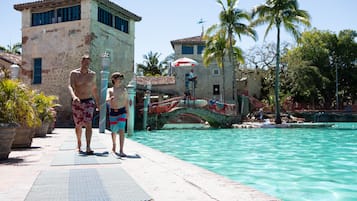 Un espace piscine agrémenté d’un chemin en pierre, d’un pont et de palmiers.