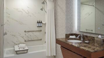A bathroom with a marble-tiled shower, a bathtub, a vanity with a sink, and a large mirror.