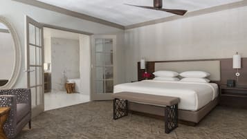 A hotel room with a large bed, a ceiling fan, a bedside table with a lamp, a mirror, and a bathroom with a toilet and sink.