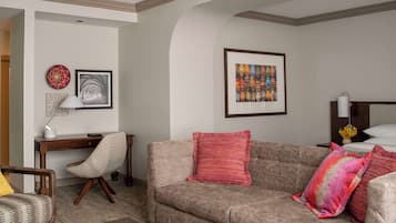 A cozy living room with a sofa, armchair, and a desk with a lamp.