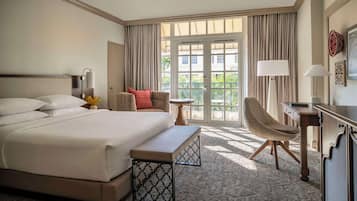 Habitación de hotel con una cama grande, un escritorio, una silla y un balcón con cortinas.