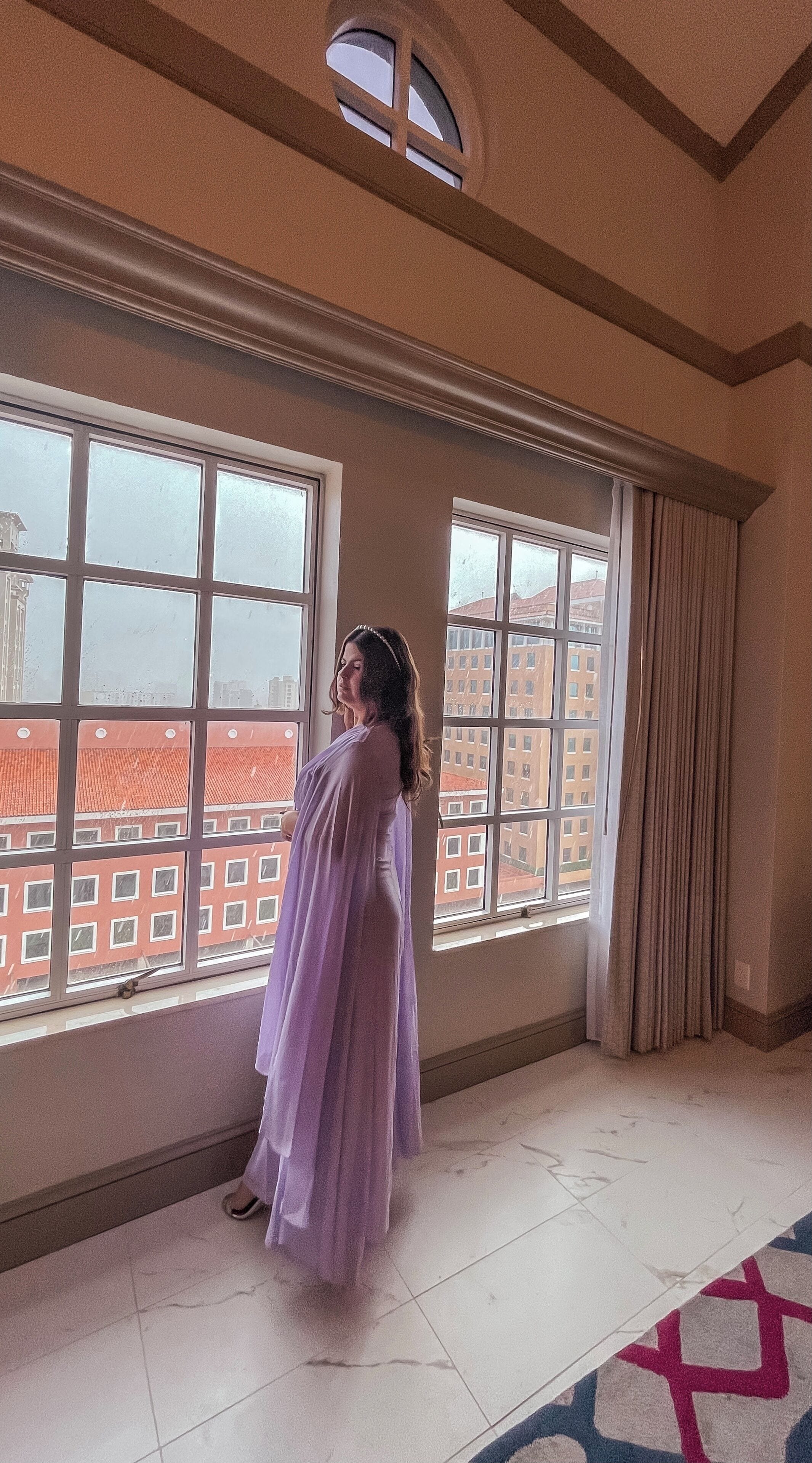 Quarto com janelas amplas, piso em azulejos e vista para prédios.