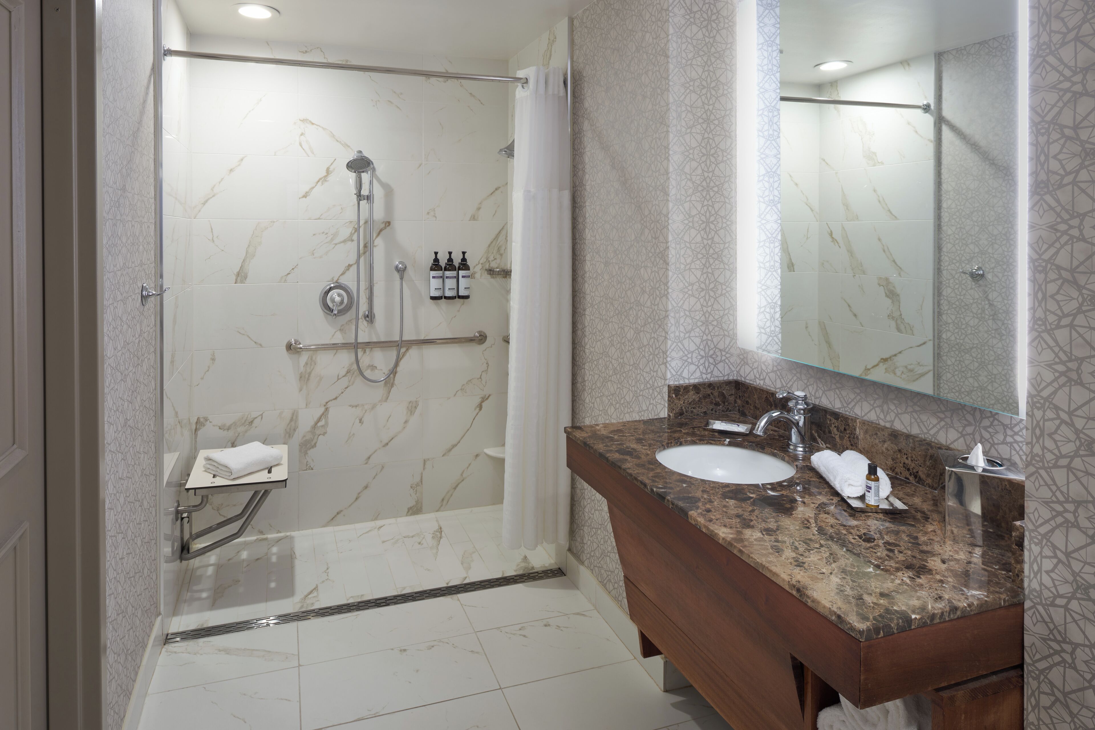 A modern bathroom with a marble shower, a vanity with a sink, and a large mirror.