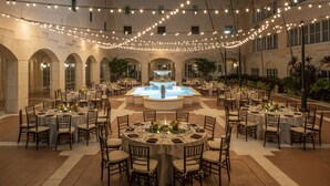 Un espace extérieur aménagé pour les repas, avec plusieurs tables rondes, des guirlandes lumineuses et une fontaine centrale.