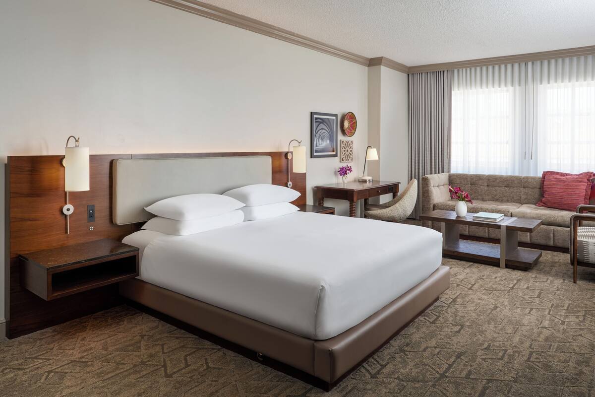 A hotel room with a large bed, a desk, a sofa, and a chair.