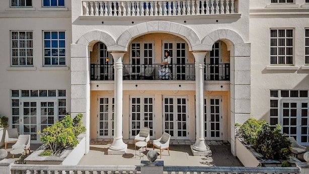 Un bâtiment à deux étages doté d’un balcon, de grandes fenêtres et d’une cour avec des sièges.