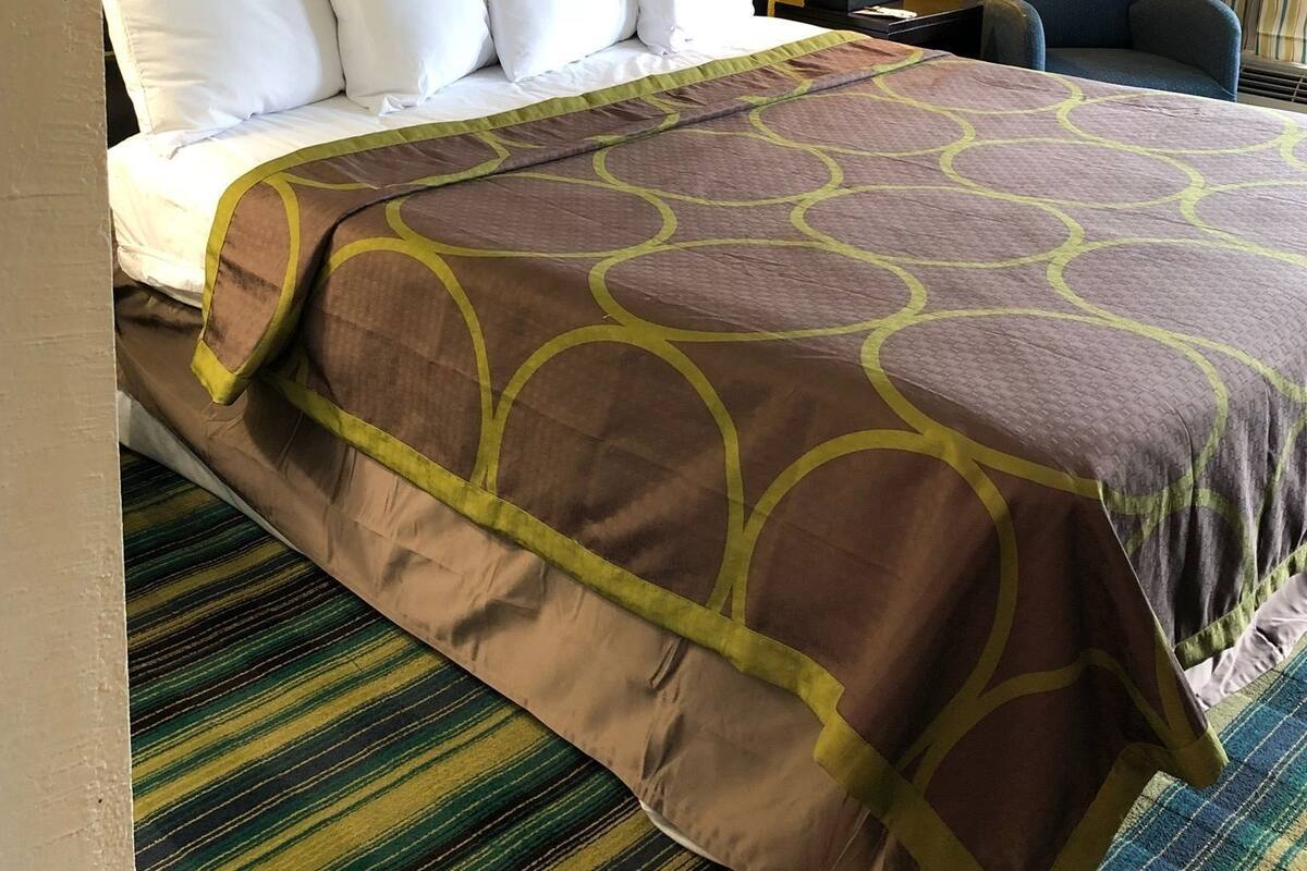 A hotel room with a bed, a desk, a chair, a lamp, and a large wall art piece.