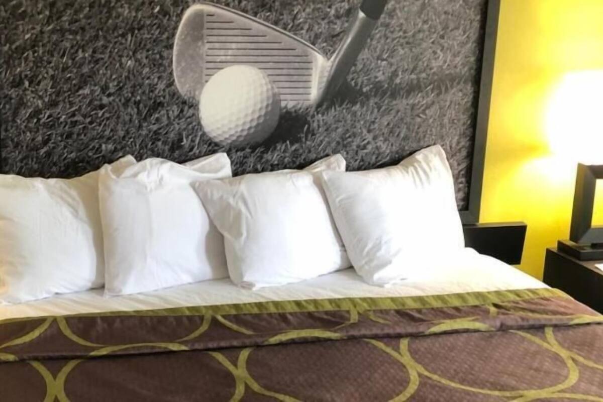 A hotel room with a bed, white pillows, a brown patterned bedspread, and a wall with a golf-themed artwork.