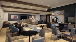 Un espacio lounge moderno con sofás, sillas, una barra de café y un refrigerador lleno de bebidas.