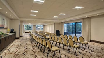 Un salón de conferencias con filas de sillas, una mesa larga y ventanas amplias.