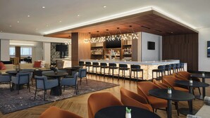 Un moderno vestíbulo de hotel con zona de bar, espacios de descanso y una pantalla de televisión.