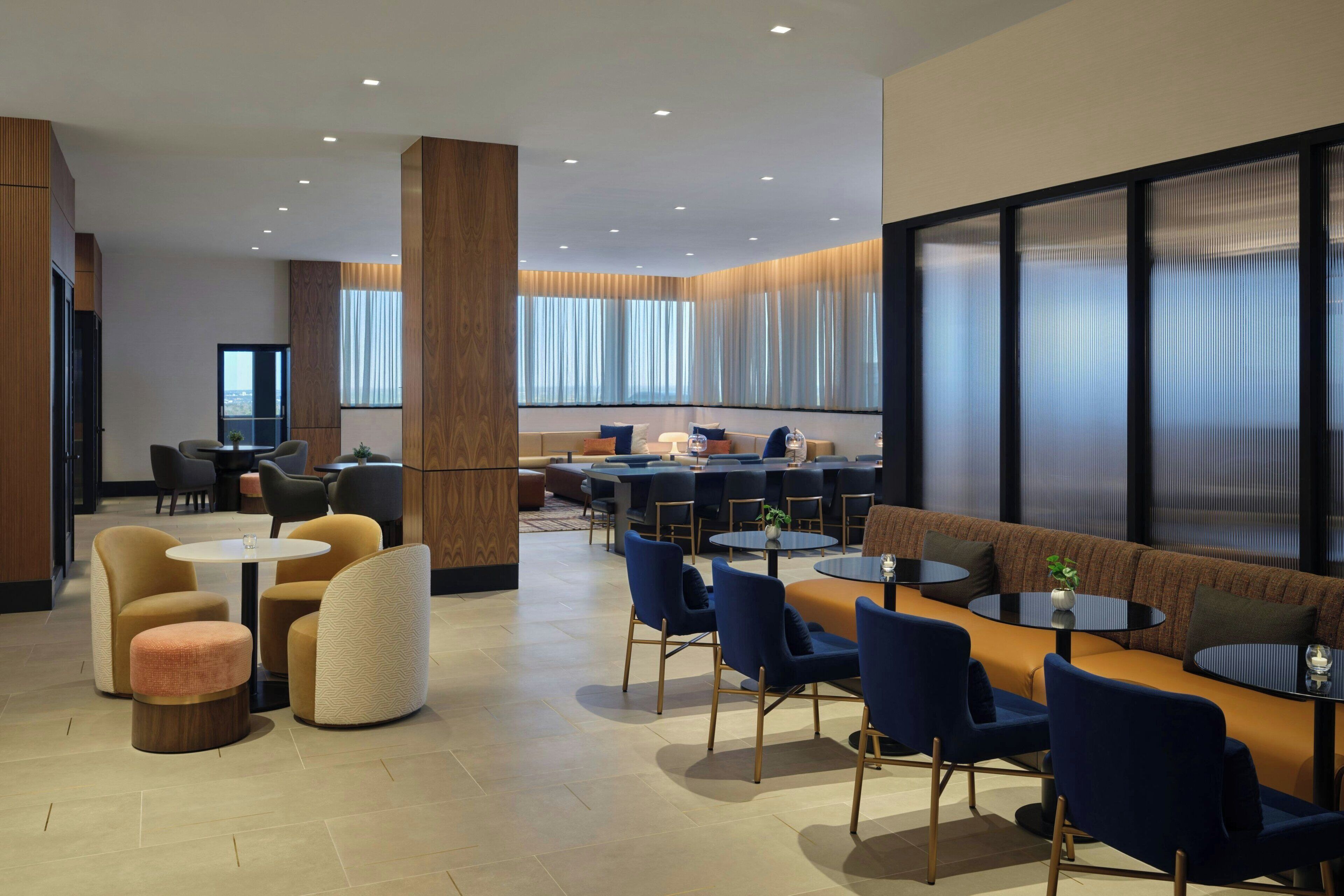 A modern hotel lobby with a seating area, a bar, and a large window with curtains.