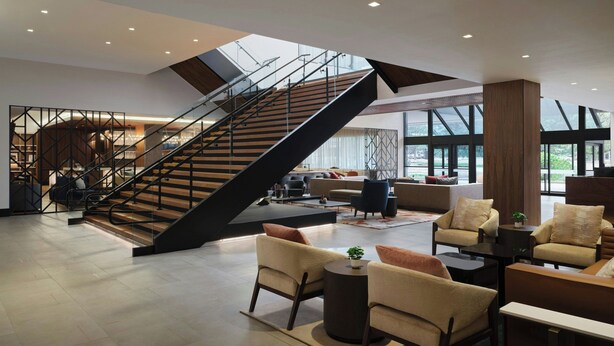 Un vestíbulo amplio con una escalera moderna, zonas de estar cómodas y ventanas grandes.