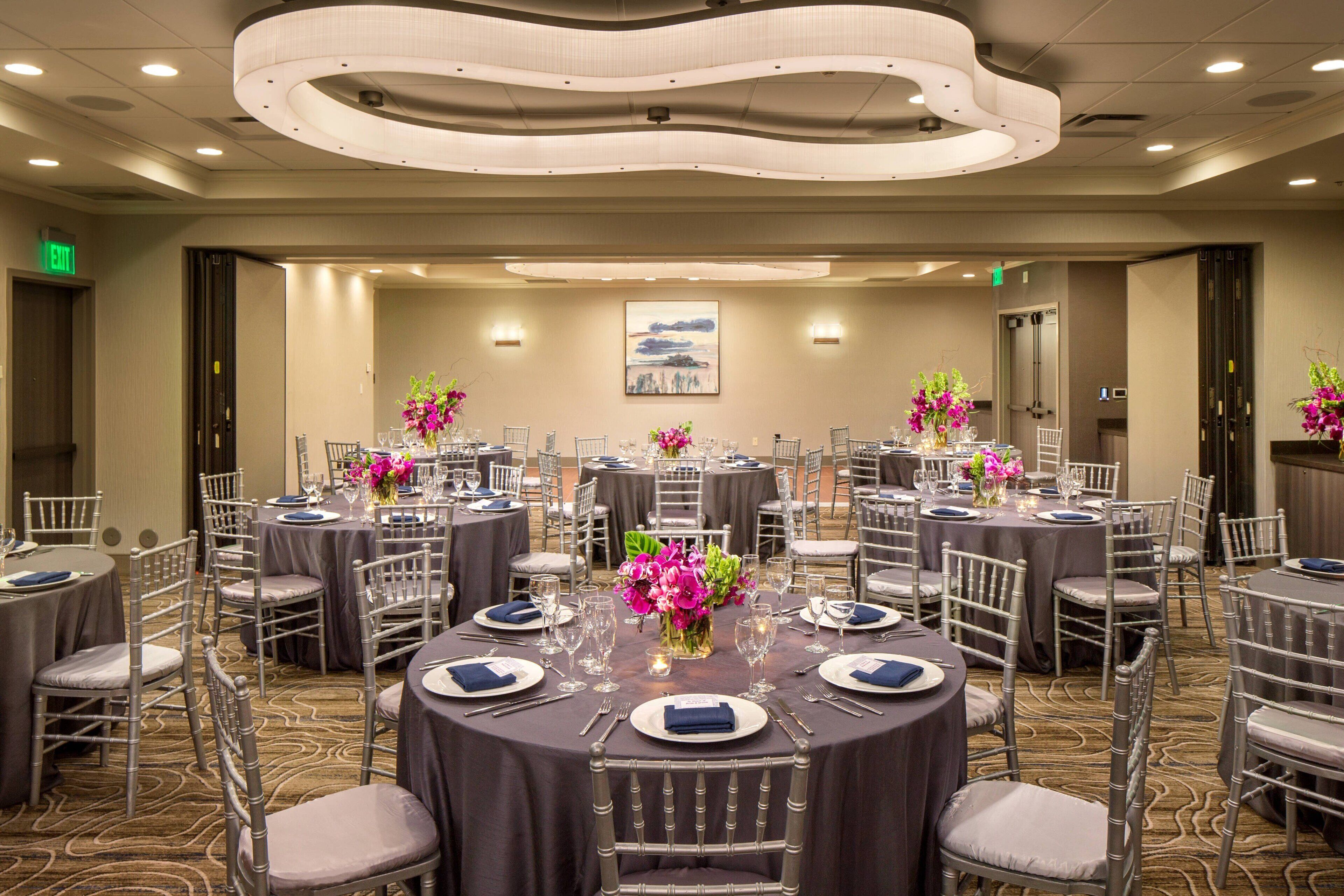A conference room with round tables, grey chairs, and floral centerpieces.