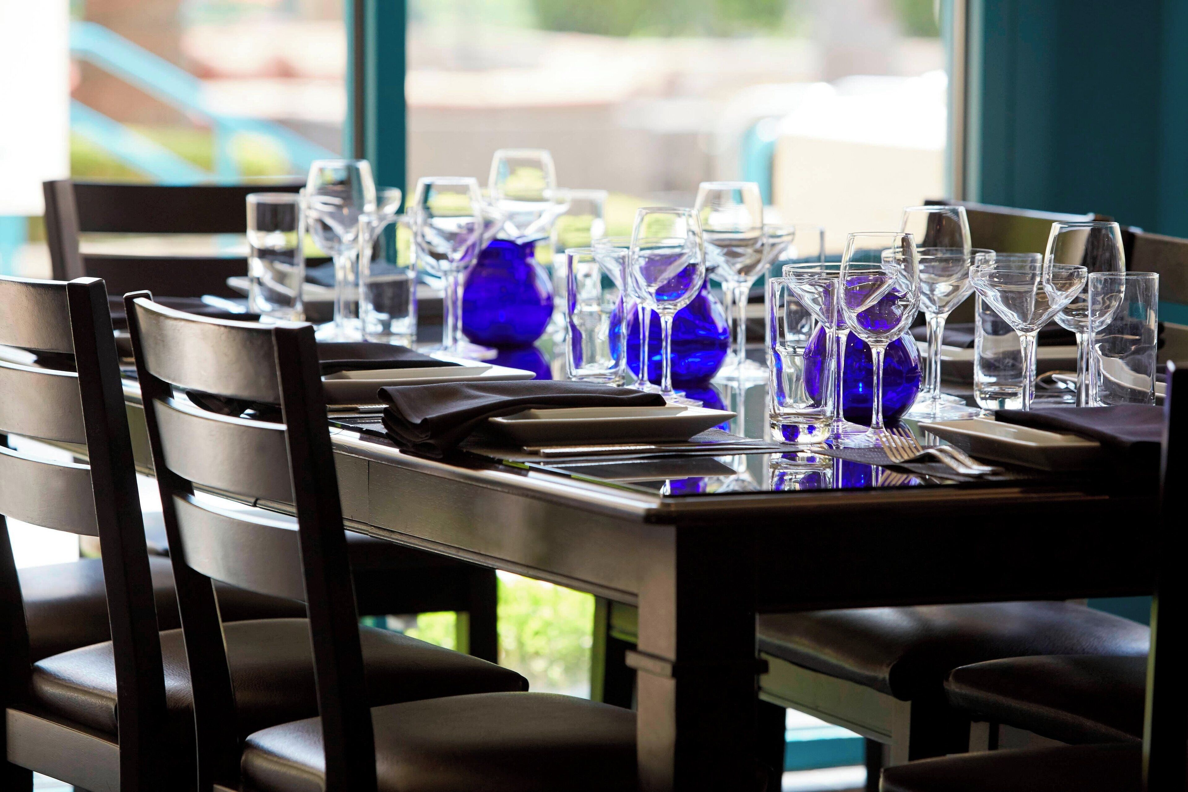 Una mesa de comedor dispuesta con sillas, vasos y un florero azul.