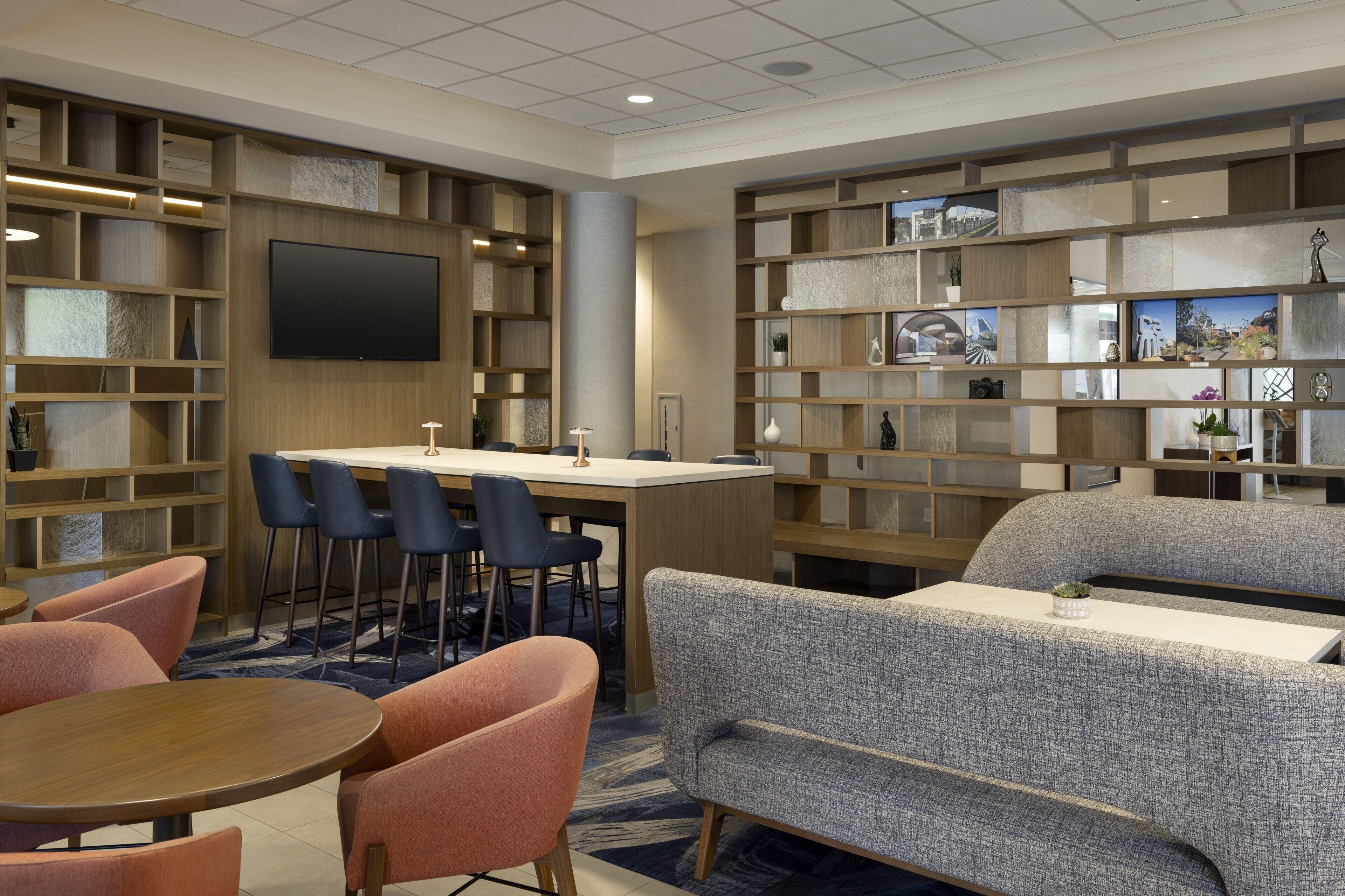 A modern hotel lobby with a bar area, seating, and a large bookshelf.