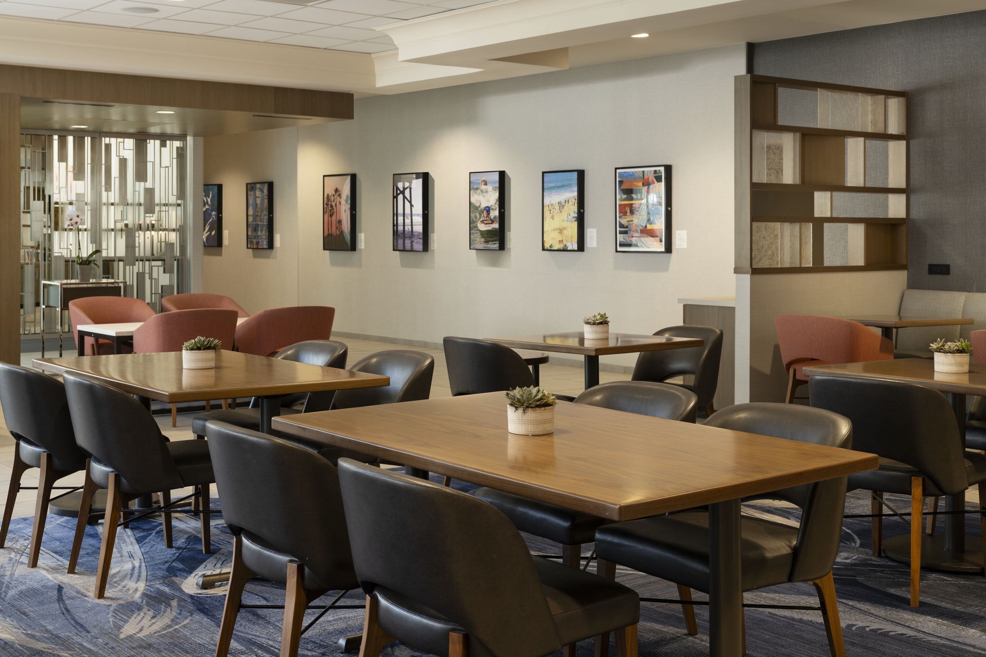 A hotel lobby with multiple seating areas, including tables and chairs, a bookshelf, and framed artwork on the walls.