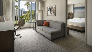 A hotel room with a sofa, a desk, a bed, and a large window with a view of palm trees and buildings. - Costa Mesa Marriott (Costa Mesa)