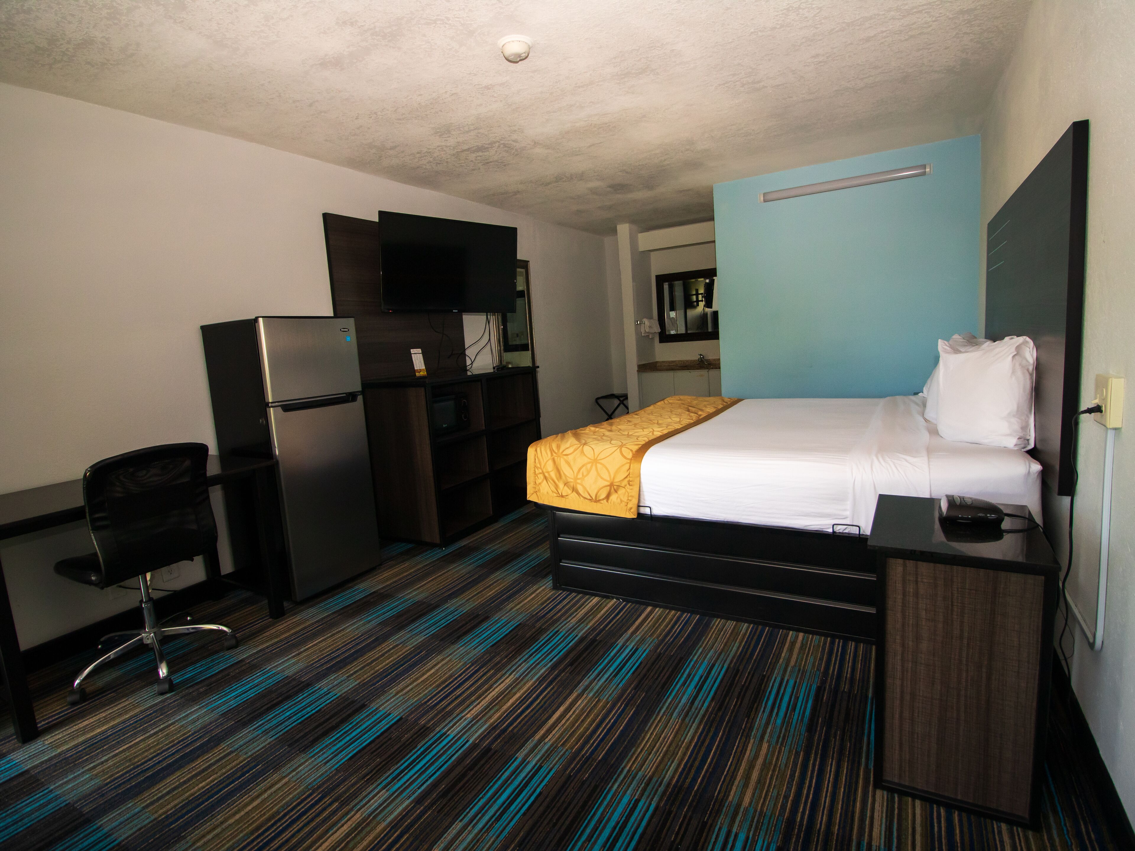 A hotel room with a bed, a desk, a chair, a refrigerator, a television, and a microwave.