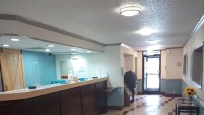 Um corredor com padrão de piso quadriculado, um balcão de recepção e uma porta que dá para outro espaço.