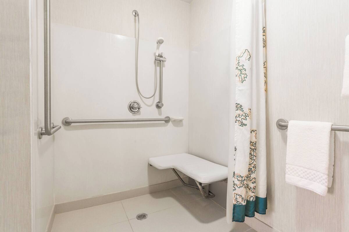 A bathroom with a shower, grab bar, bench, and a towel rack.
