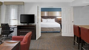 A hotel room with a bed, a desk with a TV, a chair, and a table.