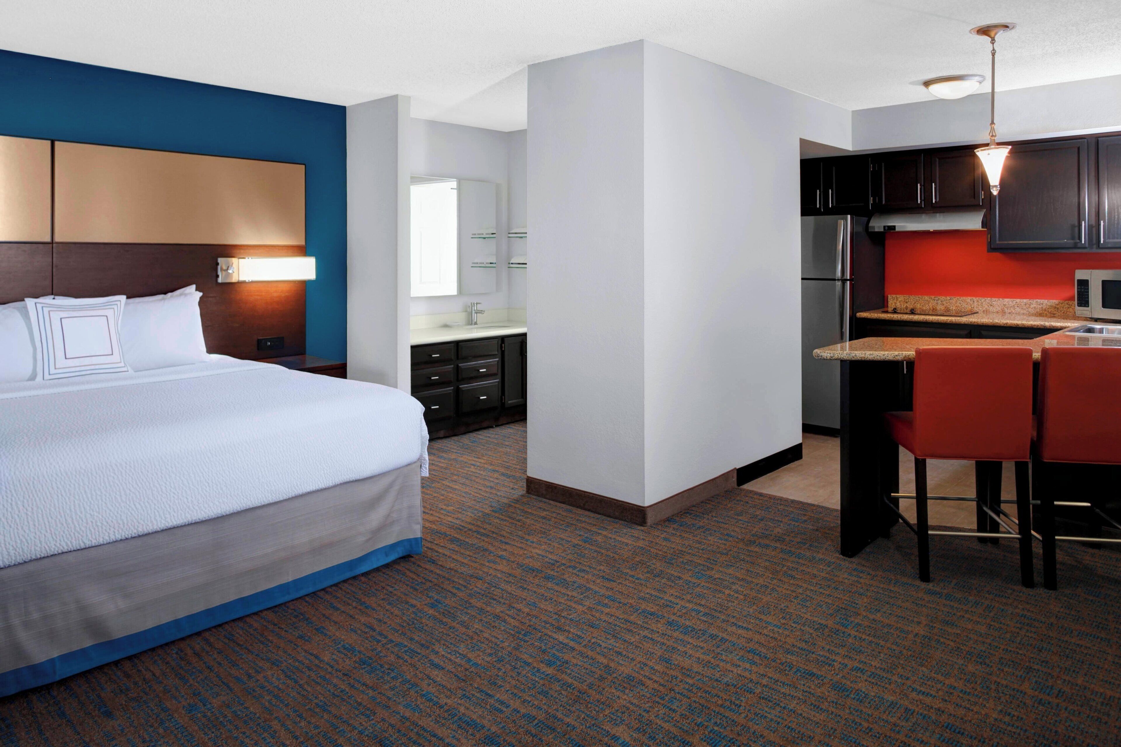 A hotel room with a bed, a kitchenette, a bathroom, and a dining area.