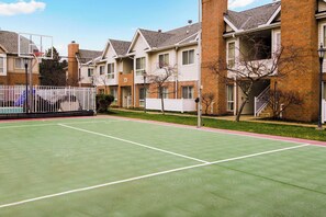 Residents can enjoy a well-maintained tennis court surrounded by apartment buildings with balconies and windows.