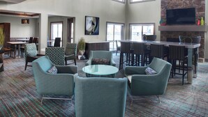 A spacious lounge area with a mix of seating options, including armchairs and a round table, and a bar area with stools.