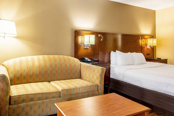 A hotel room with a sofa, a bed, a wooden table, and two bedside lamps. - Econo Lodge Naval Station Norfolk (Norfolk)