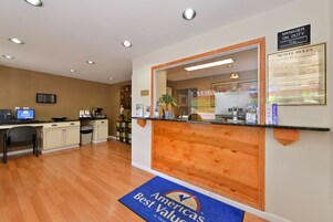 A reception area with a wooden counter, a blue mat with text, a sign indicating 'Manager on Duty', and a framed 'Motel Rules' notice.