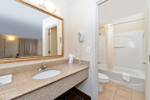 A bathroom with a granite countertop sink, a mirror, a hairdryer, and a bathtub.