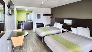 Habitación de hotel con dos camas, una mesa de comedor, una silla, un microondas y una pequeña cocina americana.