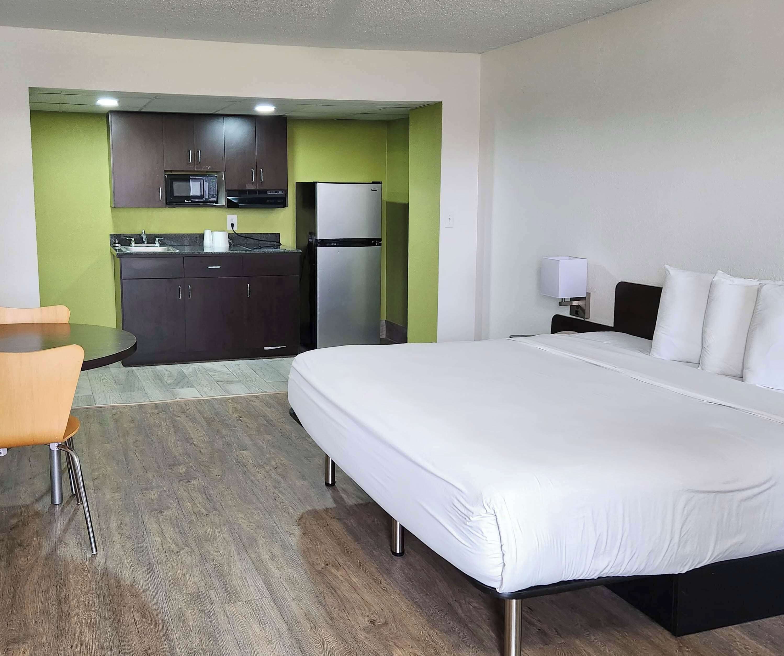 Une chambre d’hôtel comprenant un lit, un bureau, une chaise, une kitchenette équipée d’un four à micro-ondes et d’un réfrigérateur, ainsi qu’une table de chevet avec une lampe.