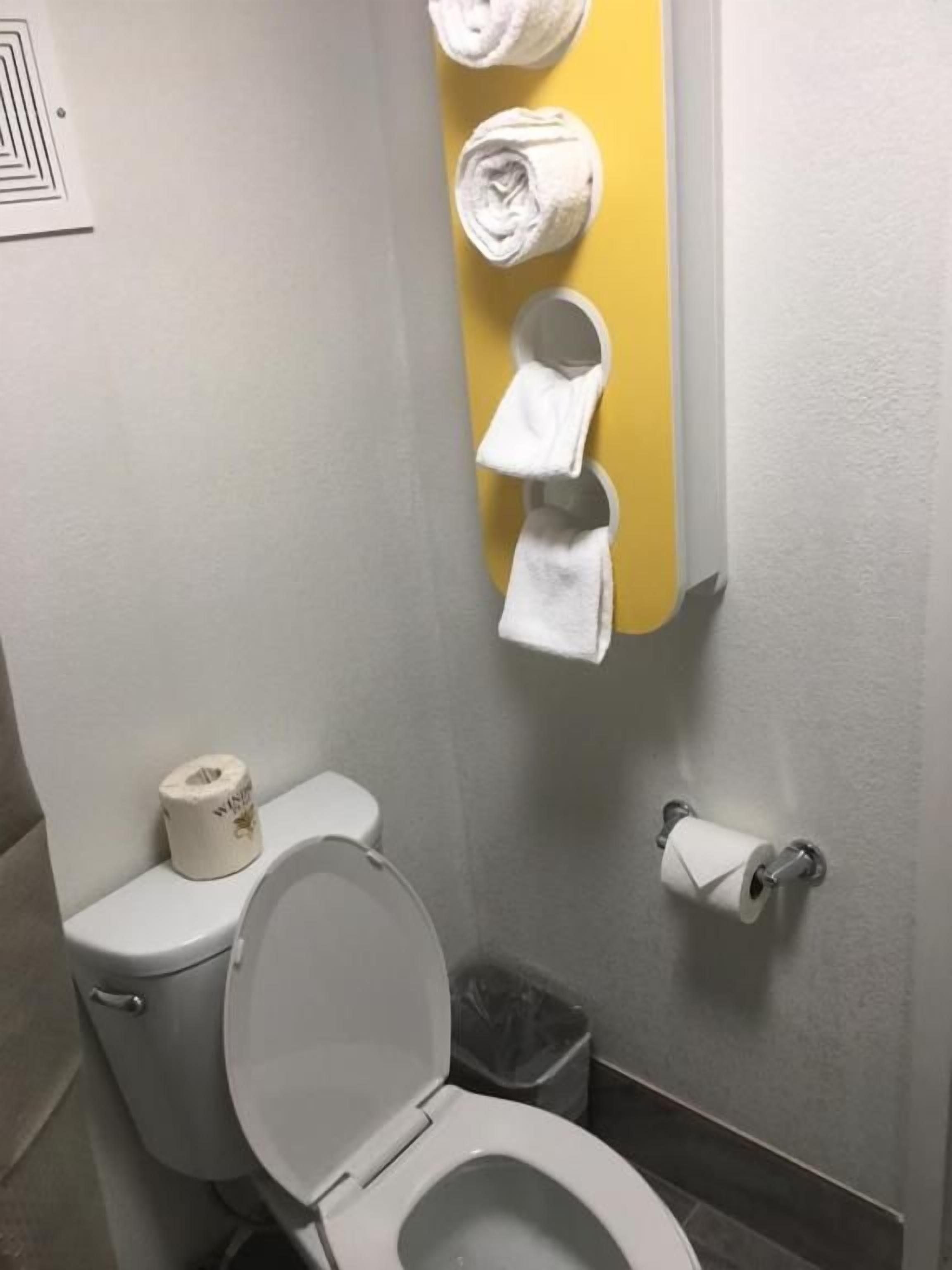 Une salle de bain équipée de toilettes, d’une poubelle et d’un porte-serviettes avec des serviettes.