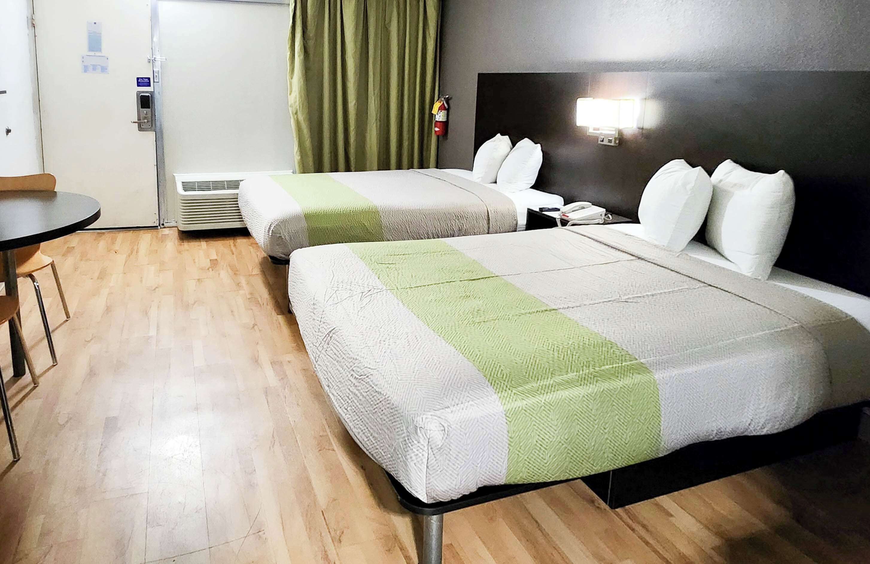 Ein Hotelzimmer mit zwei Betten, einem kleinen Tisch, einem Stuhl, einem an der Wand befestigten Telefon und einem Feuerlöscher.