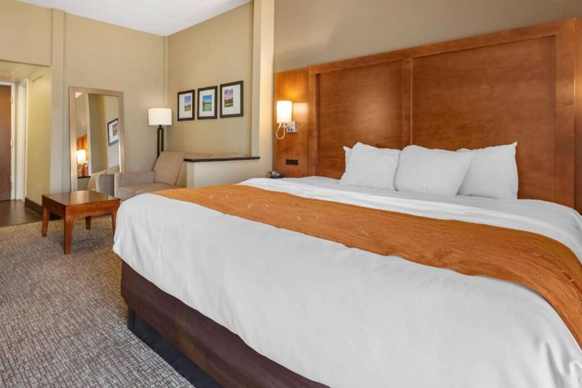 A hotel room with a large bed, a desk, a chair, a lamp, and framed pictures on the wall.