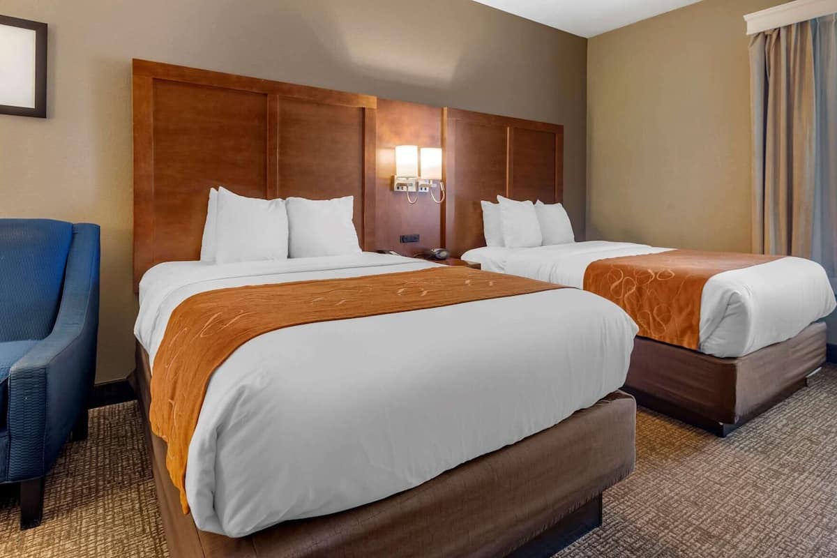 A hotel room with two beds, a blue chair, and a wooden headboard.
