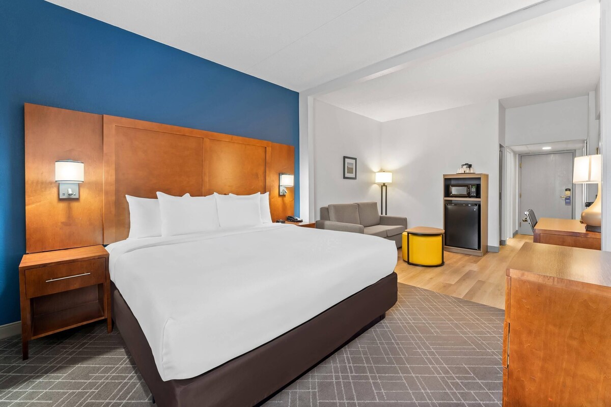 Habitación de hotel con una cama grande, mesitas de noche, un escritorio, una silla, microondas y refrigerador.