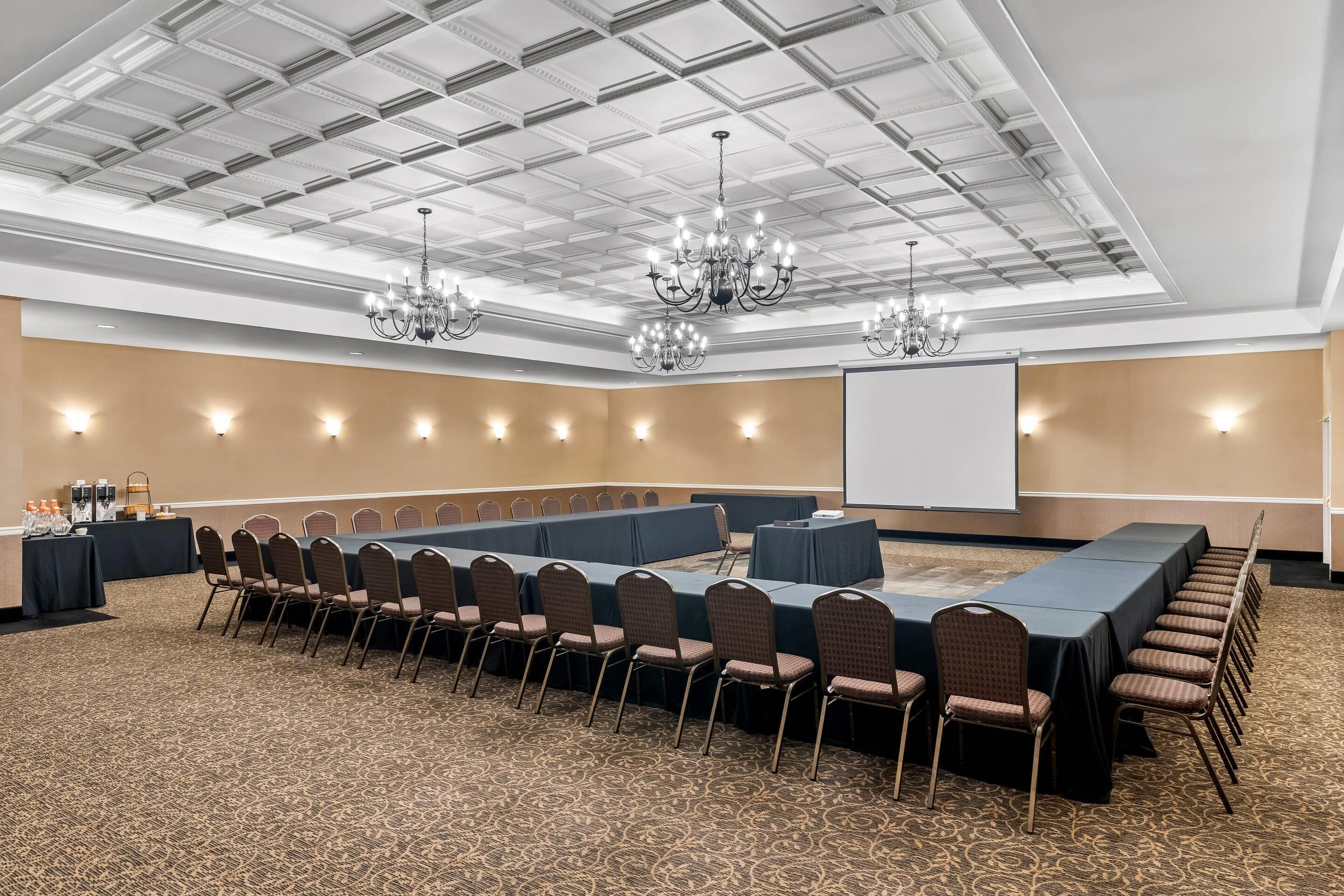 A conference room with a long table, chairs, a projector screen, and chandeliers.