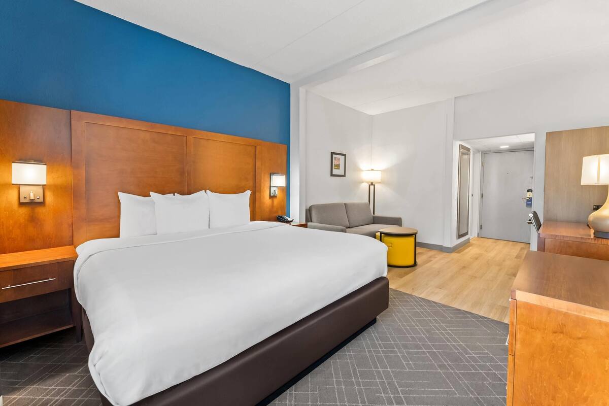 A hotel room with a large bed, a wooden headboard, a desk, a chair, and a small table.