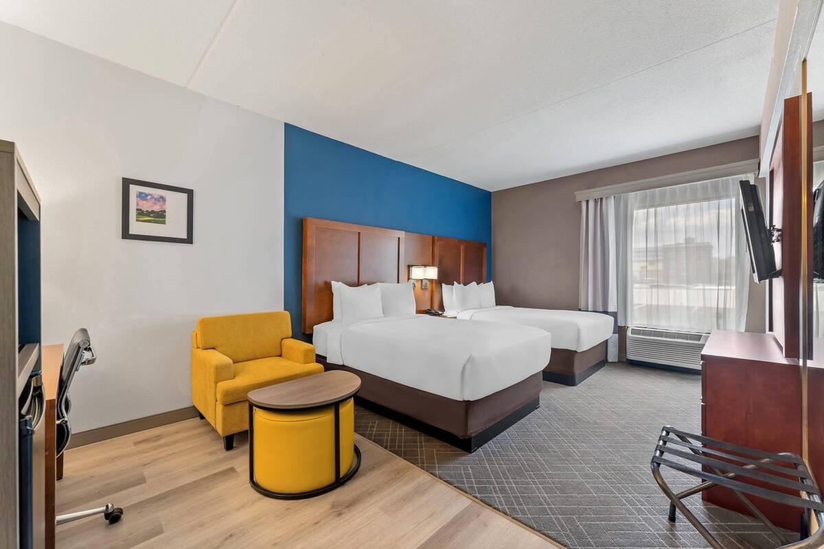 A hotel room with a bed, two bedside tables, a chair, a desk, and a window with curtains.