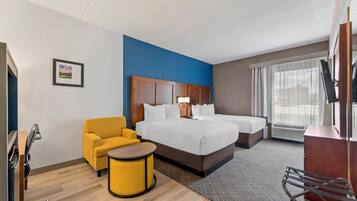 Quarto de hotel com cama, duas mesas de cabeceira, uma cadeira, escrivaninha e janela com cortinas.