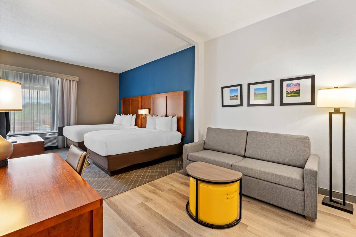 A hotel room with a bed, a sofa, a small table, and a lamp.