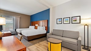 Una habitación de hotel con cama, sofá, una mesita y una lámpara.