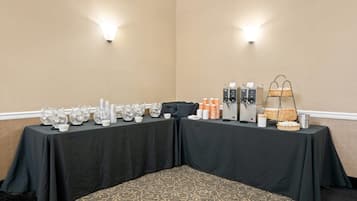 Ein Konferenzraum mit zwei Tischen, beide mit schwarzen Tischdecken bedeckt, ausgestattet mit Gläsern, Tassen und einer Kaffeemaschine.