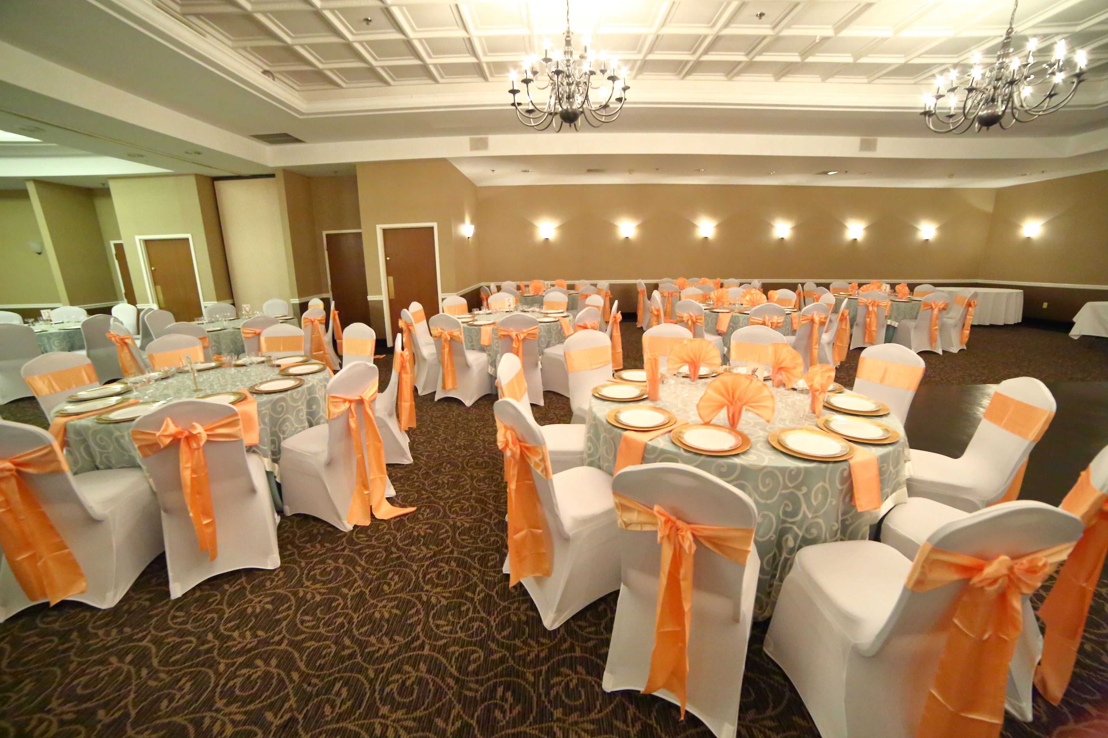 Une salle de banquet avec des tables rondes, des chaises blanches ornées de rubans orange et des lustres.
