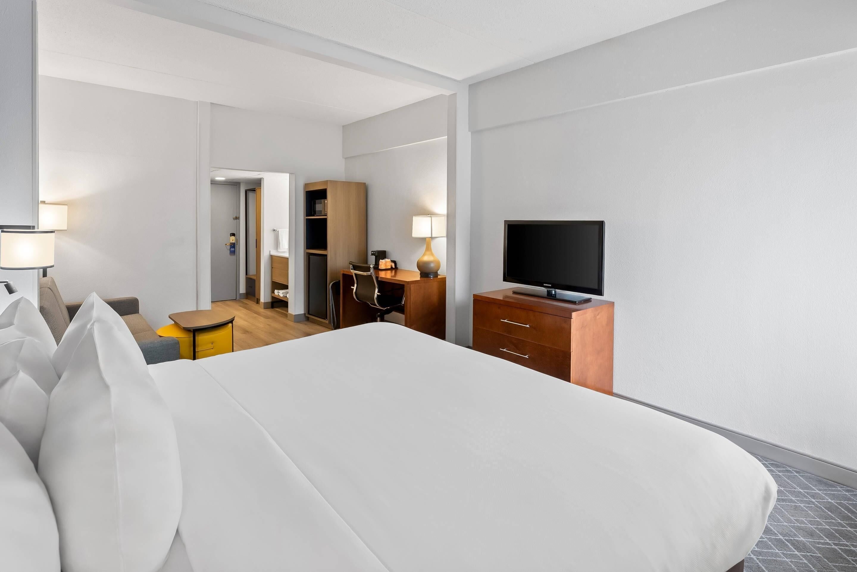 Habitación de hotel con cama, televisión, escritorio, silla, lámpara y armario.