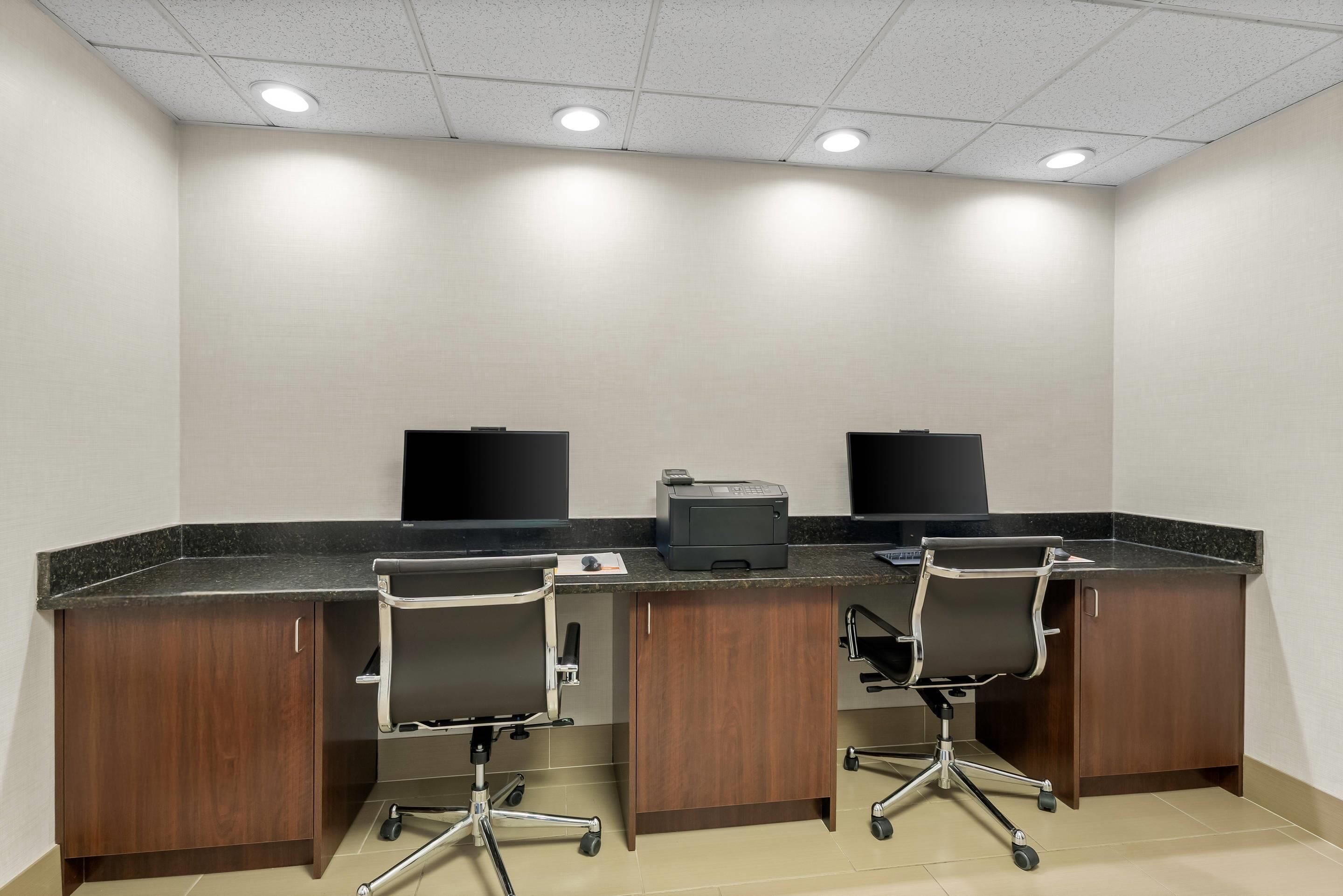 A conference room with two desks, chairs, a printer, and a black screen on each desk.