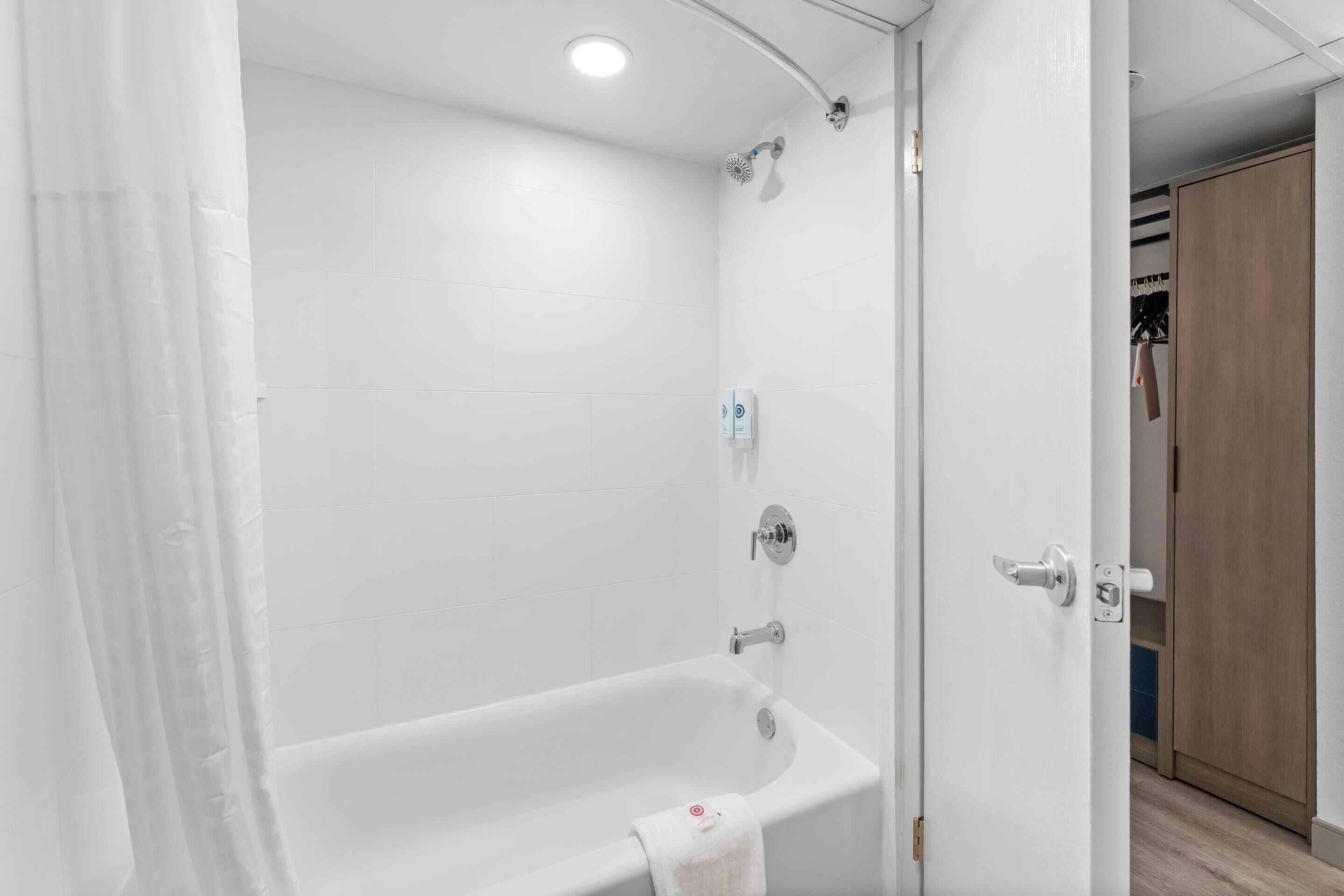 Un baño blanco con bañera, ducha y una puerta que da a un vestidor.